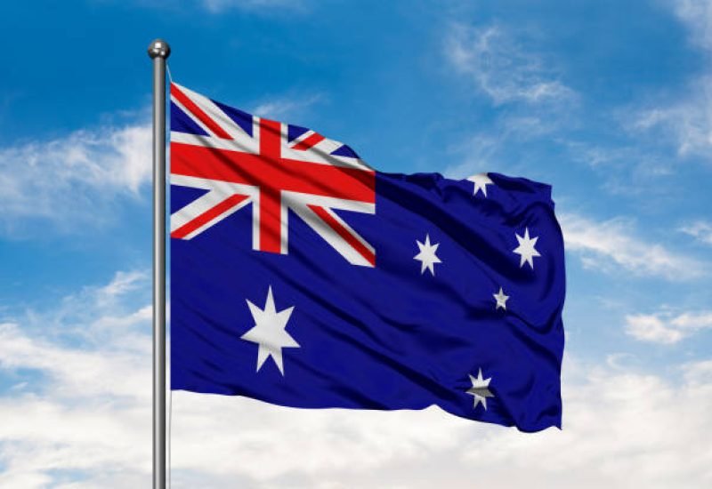 Flag of Australia waving in the wind against white cloudy blue sky. Australian flag.